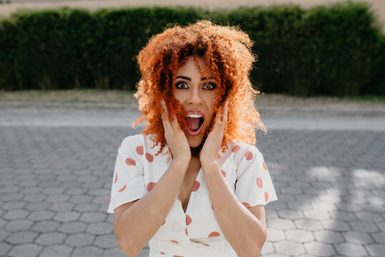 Surprised young woman with mouth open standing on footpath