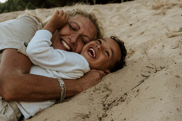 Grandmother and grandson embracing each other while lying down on sand at beach during sunset