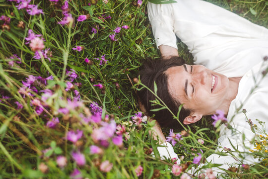 Cheerful woman with eyes closed lying amidst plants on land