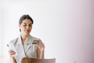 Smiling businesswoman holding credit card while using mobile phone at office