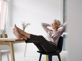 Businesswoman with hands behind head relaxing on chair in loft office