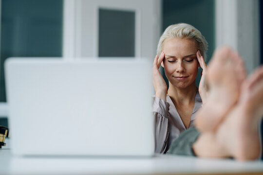 Businesswoman with head in hands relaxing by laptop at desk at office
