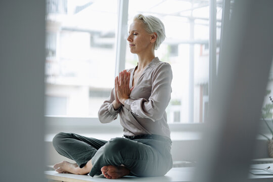 Businesswoman with eyes closed meditating while sitting against window in loft office