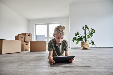 Boy lying down while playing on digital tablet in new house