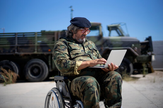 Army soldier using laptop while sitting on wheelchair against military truck during sunny day