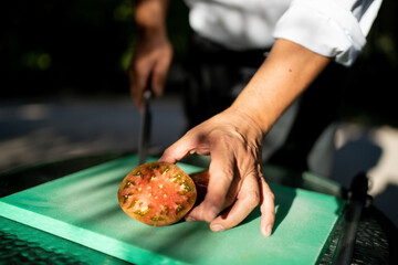 Close-up of male chef holding tomato slice on cutting board in orchard
