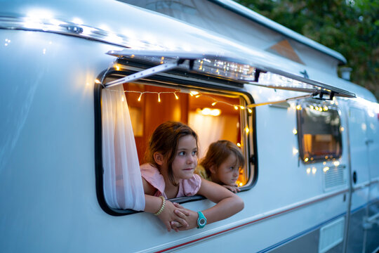 Cute sisters looking through window of illuminated motor home at dusk