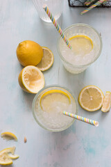 Overhead view of two lemonade glasses with two colorful straws inside. Some slices and half lemons are around them.