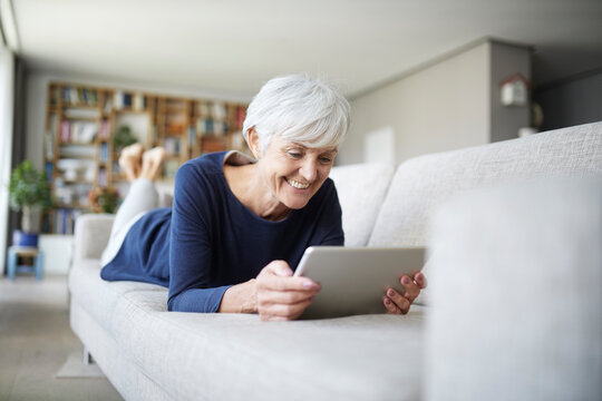 Senior Woman Using Digital Tablet Lying On Sofa At Home