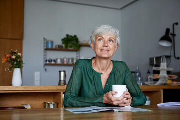 Thoughtful senior woman sitting with coffee cup at home