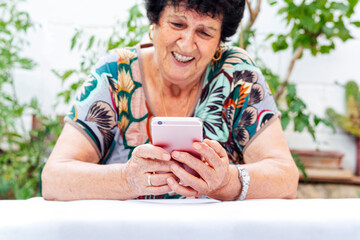 Close-up of smiling senior woman using mobile phone at table while sitting in yard