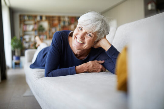 Smiling senior woman with head in hand lying on sofa at home