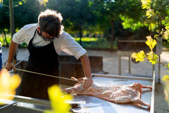 Male chef wearing mask cutting goat meat on table while standing in orchard