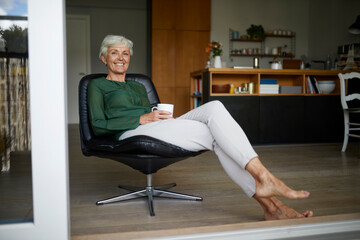 Senior woman spending leisure time while drinking coffee at home