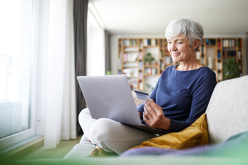 Senior woman using credit card while doing online shopping on laptop at home