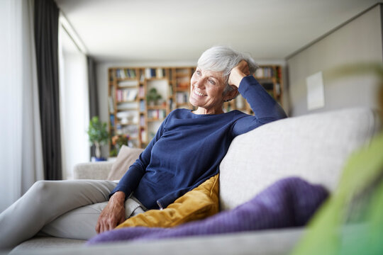 Smiling senior woman with head in hand sitting on sofa at home