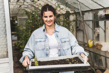 Smiling young woman holding tray while standing in greenhouse
