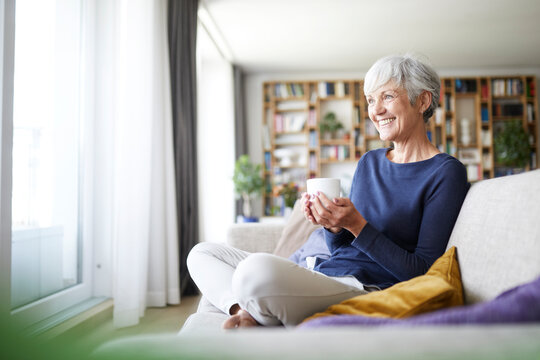 Smiling woman holding coffee cup while sitting on sofa at home
