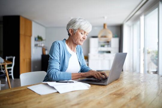 Senior woman working on laptop while sitting on chair at home