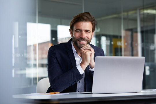 Smiling businessman using laptop while sitting on chair in office