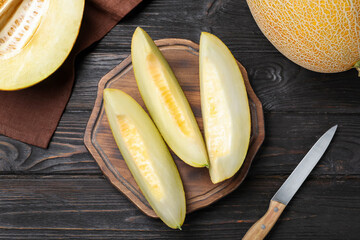 Pieces of delicious honeydew melon on black wooden table, flat lay