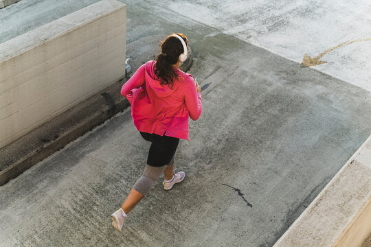 Female athlete listening music over headphones while running on terrace at sunset