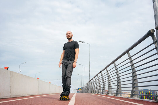 Smiling young man looking away while inline skating on bridge against cloudy sky