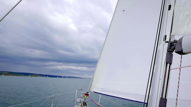 View Of Headsail (Jib) And Mast Of A Sailboat Sailing On The Calm Blue Sea - panning down shot