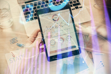 Double exposure of man's hands holding and using a digital device and forex graph drawing. Financial market concept.