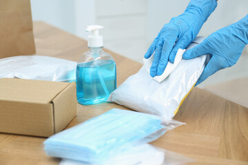 Woman cleaning parcel with wet wipe at wooden table, closeup. Preventive measure during COVID-19 pandemic