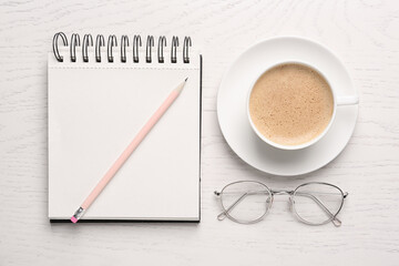 Notebook with pencil, glasses and cup of coffee on white wooden table, flat lay