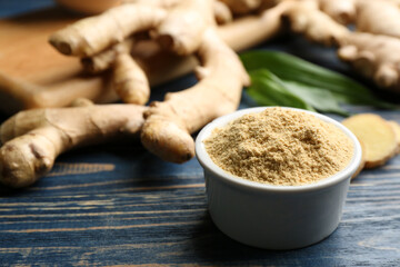 Dry ginger powder in bowl and fresh root on blue wooden table