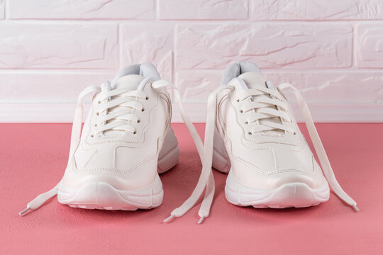 Pair Of White Chunky Sole Sneakers On A Pink Coral Colored Floor. New Female Or Teen Untied Laces Shoes For Active Lifestyle, Fitness And Sports.