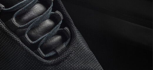 Black sneaker shoe from mesh on a dark background. Closeup of laces and leather tab. - obrazy, fototapety, plakaty