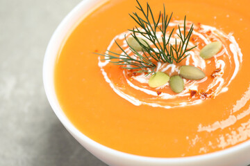 Delicious pumpkin soup in bowl on grey table, closeup