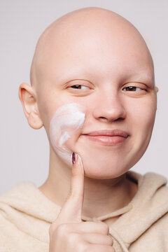Happy woman with alopecia applying cream on face