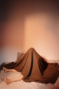 Woman sitting on bed under blanket