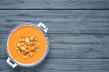 Tasty creamy pumpkin soup with croutons and seeds in bowl on blue wooden table, top view. Space for text