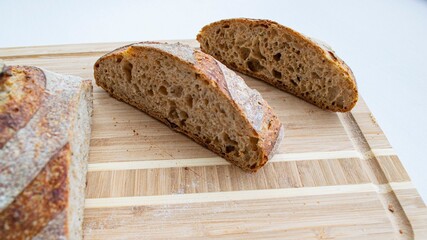 Pieces of homemade whole grain rye bread on a wooden board (on the object on the left the focus is specially blurred), on a gray background