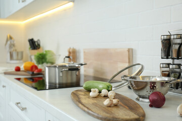Fresh vegetables and mushrooms on white countertop in modern kitchen. Space for text