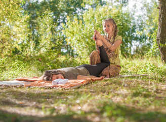 Proffesional masseuse applies her massage skills on her client on the grass of the forest.