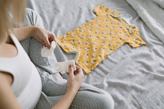 Pregnant Mother Sitting On Bed With Baby clothes