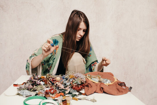 Focused woman working with embroidery at messy table