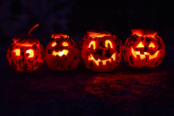 row of four carved bumpy pumpkin Jack O Lanterns lit by candles within at night