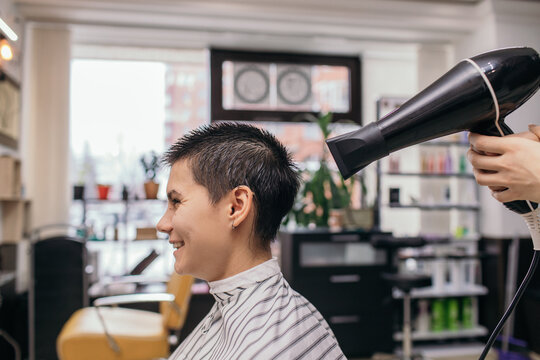 Crop hairstylist drying hair of cheerful androgynous customer