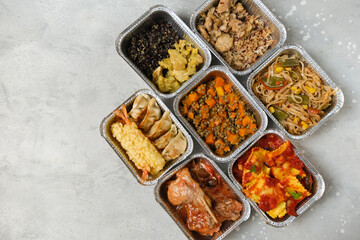 Food delivery. Different aluminium lunch box with ravioli, curry chicken  rice, gyoza tempura, noodles vegetables, lentils with pumpkin . airlines meals and snacks. takeaway takeout coronavirus food