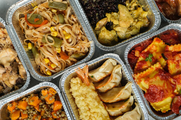 Food delivery. Different aluminium lunch box with ravioli, curry chicken  rice, gyoza tempura, noodles vegetables, lentils with pumpkin . airlines meals and snacks. takeaway takeout coronavirus food