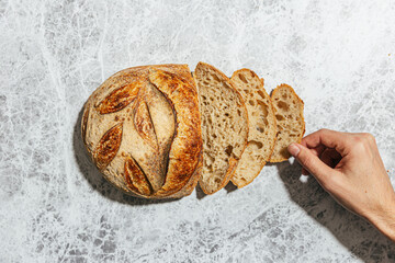 Loaf of sourdough bread with hand holding one slice