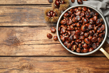 Delicious roasted edible chestnuts on wooden table, flat lay. Space for text