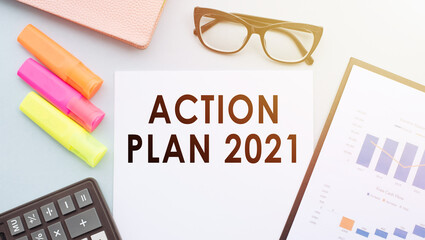 The text Action Plan 2021 on office desk with calculator, markers, glasses and financial charts